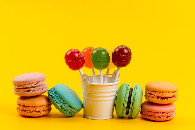 Französische Macarons von oben mit Lutschern und bunten Bonbons verteilen sich auf gelben, zuckersüßen Süßwaren