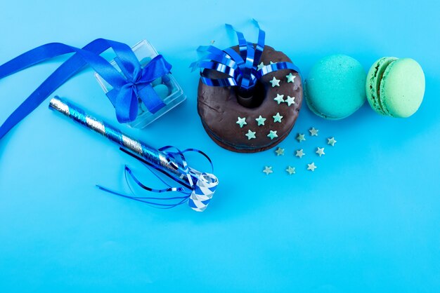 Französische Macarons von oben mit Schokoladenkrapfen und Partydekorationen auf blauer, süßer Bsicuit-Kuchenfarbe