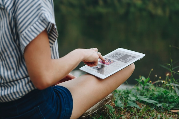 Frau alleine in der Natur, die eine digitale Tablette mit Unterhaltungsanwendung auf dem Schirminternet c verwendet