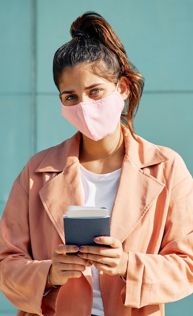 Frau am Flughafen während der Pandemie mit medizinischer Maske und Pass