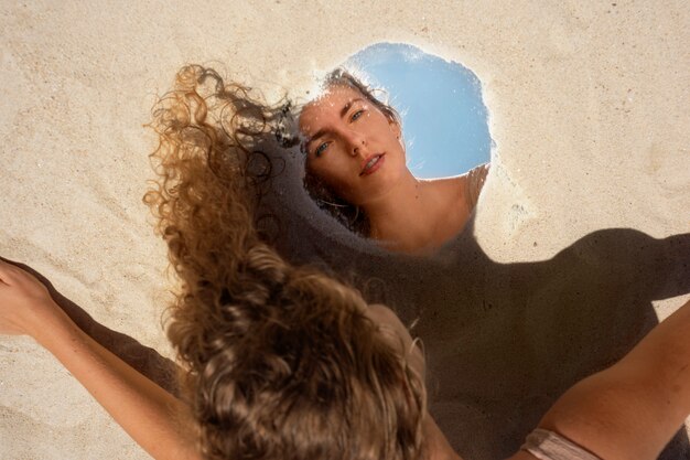 Frau am Strand im Sommer posiert mit rundem Spiegel