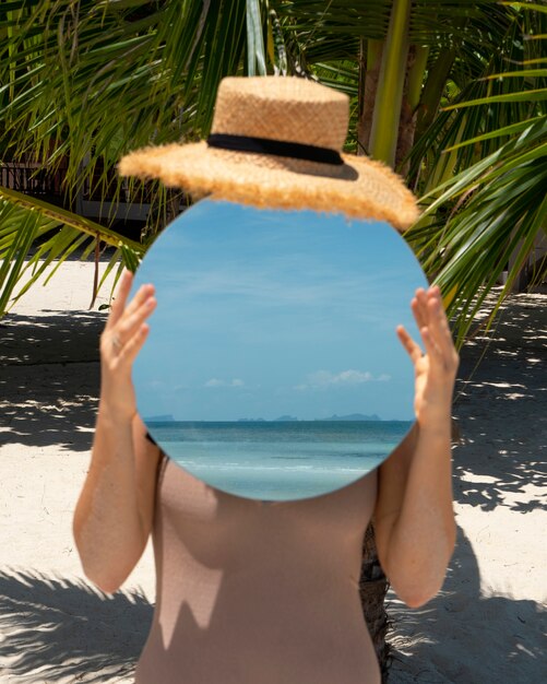 Frau am Strand im Sommer posiert mit rundem Spiegel