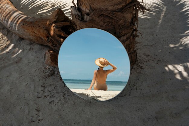 Frau am Strand im Sommer posiert mit rundem Spiegel