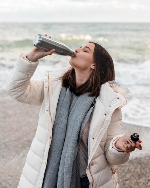 Frau am Strand mit einem Getränk aus der Flasche