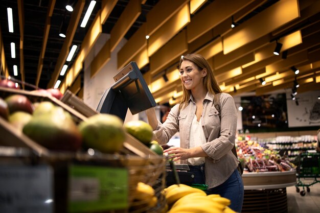 Frau am Supermarkt, der Selbstbedienungs-Digitalwaage verwendet, um das Gewicht von Obst zu messen