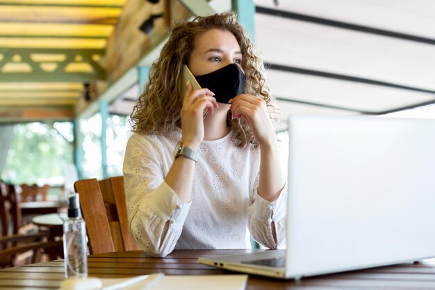 Frau an der Terrasse mit Maske, die über Telefon spricht