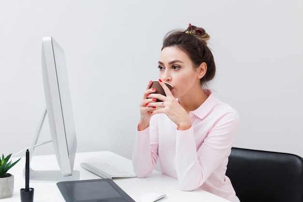 Frau an trinkendem Kaffee des Schreibtisches und am Betrachten des Computers