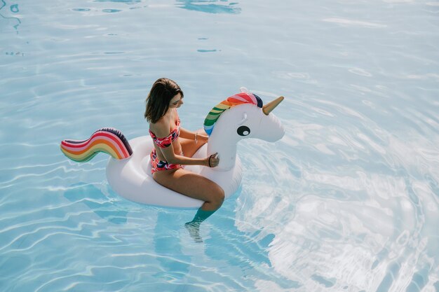 Frau auf aufblasbarem Einhorn im Pool