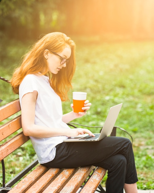 Kostenloses Foto frau auf bank mit laptop und getränk