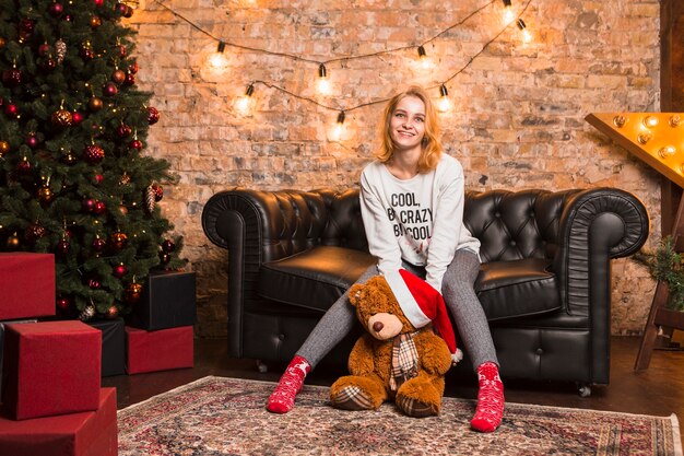 Frau auf Couch mit tragendem Weihnachtshut des Teddybären