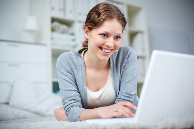 Frau auf dem Boden liegend und tippen auf dem Laptop