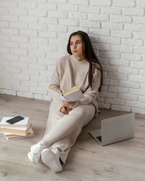 Frau auf dem Boden mit Buch und Laptop