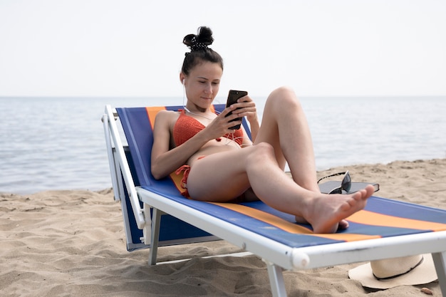 Frau auf dem Strandstuhl, der Telefon betrachtet