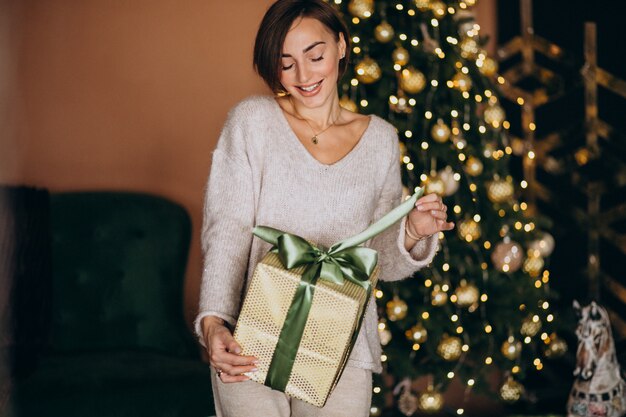 Frau auf dem Weihnachten, das ein Weihnachtsgeschenk durch den Weihnachtsbaum hält