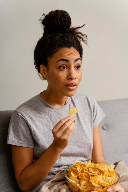 Frau auf der Couch, die fernsieht und Chips isst