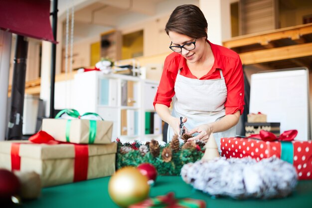Frau bei der Arbeit, einen Weihnachtskranz machend und Geschenke einpackend