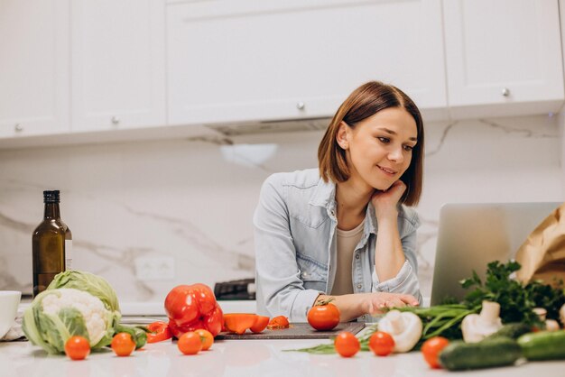 Frau bereitet Abendessen in der Küche zu und schaut sich Rezepte online an