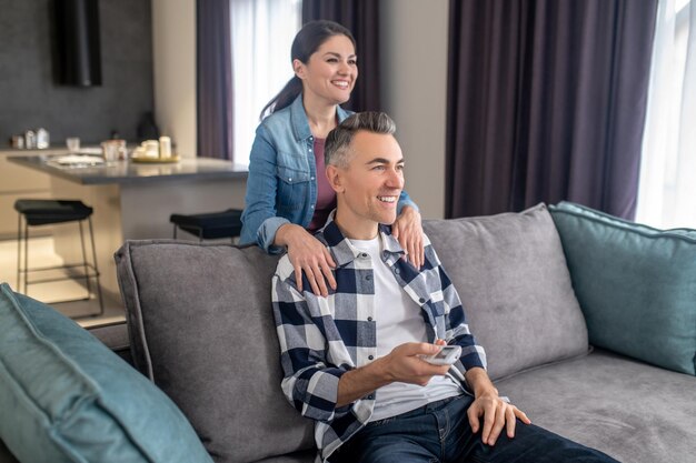 Frau berührt die Schultern eines Mannes, der auf der Couch sitzt