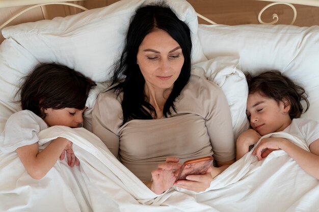 Frau checkt ihr Smartphone, während ihre Zwillinge schlafen