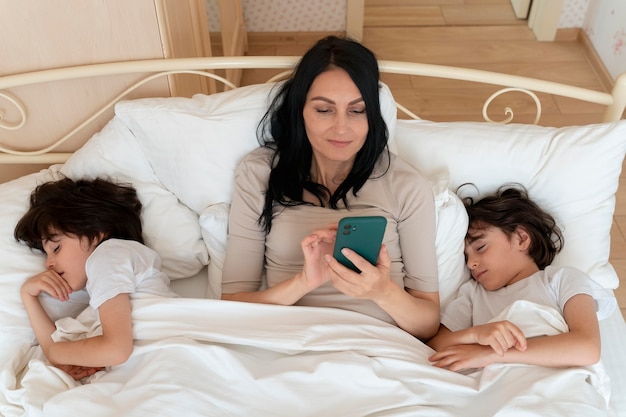 Frau checkt ihr Smartphone, während ihre Zwillinge schlafen