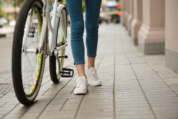 Frau der Ansicht von unten, die nahe bei Fahrrad geht