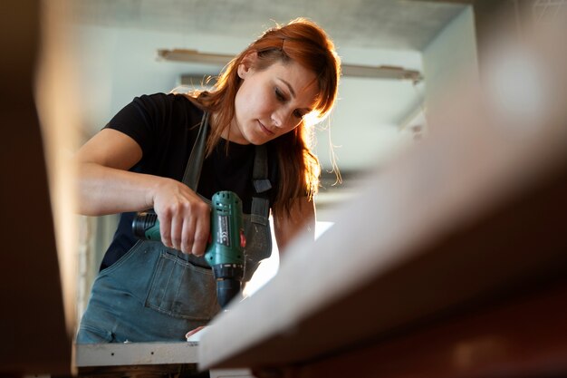 Frau des niedrigen Winkels, die mit Bohrmaschine arbeitet