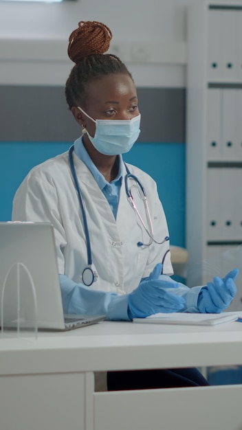 Frau, die als Medizinerin arbeitet und mit einem alten, ungültigen Mann im medizinischen Kabinett in der Gesundheitsklinik chattet. Arzt behandelt älteren Patienten mit Behinderung und Krankheit im Rollstuhl hinter Plexiglaswand