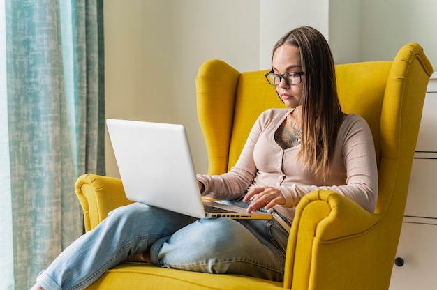 Frau, die am Laptop vom Sessel zu Hause während der Pandemie arbeitet