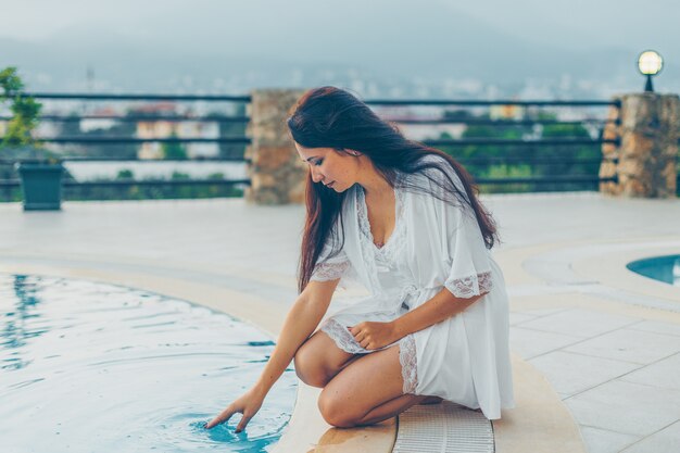 Frau, die am Pool sitzt und tagsüber im Hauskleid im Haus Wasser berührt