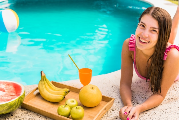 Frau, die am Rand des Pools mit Früchten liegt