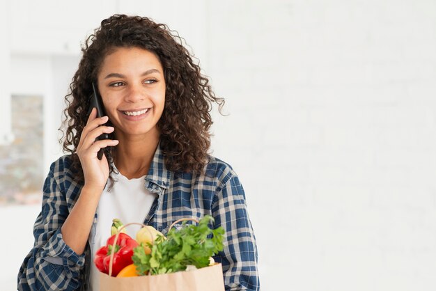 Frau, die am Telefon spricht und eine Papiertüte hält