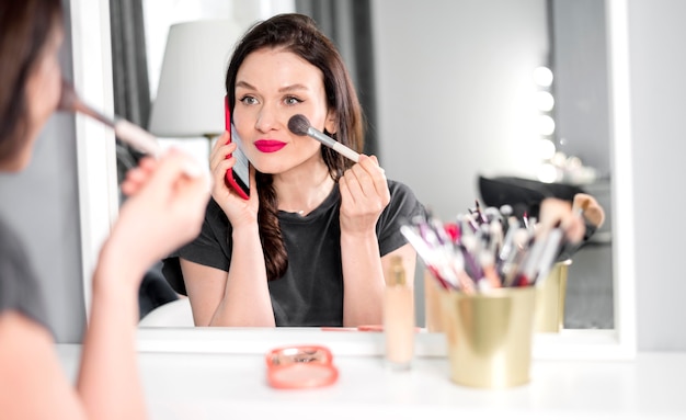 Frau, die am Telefon spricht und Make-up macht