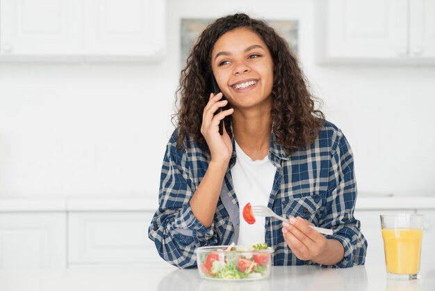 Frau, die am Telefon spricht und Salat isst