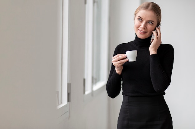 Frau, die am Telefon spricht und Tasse Kaffee hält