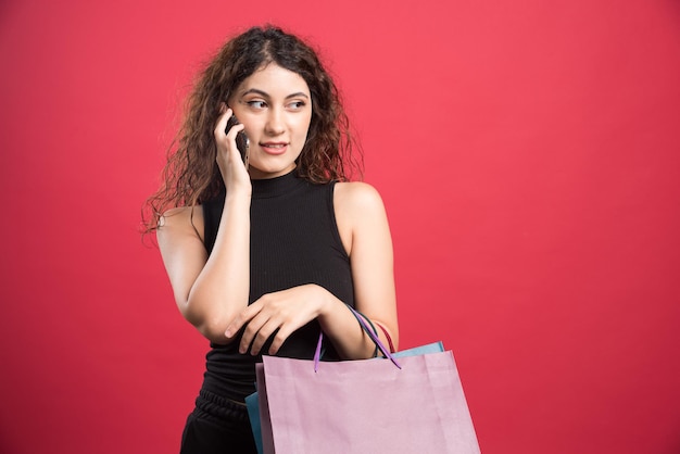 Frau, die am Telefon spricht und viele Taschen auf Rot hält.