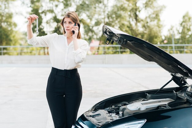 Frau, die am Telefon und am schwarzen Auto spricht