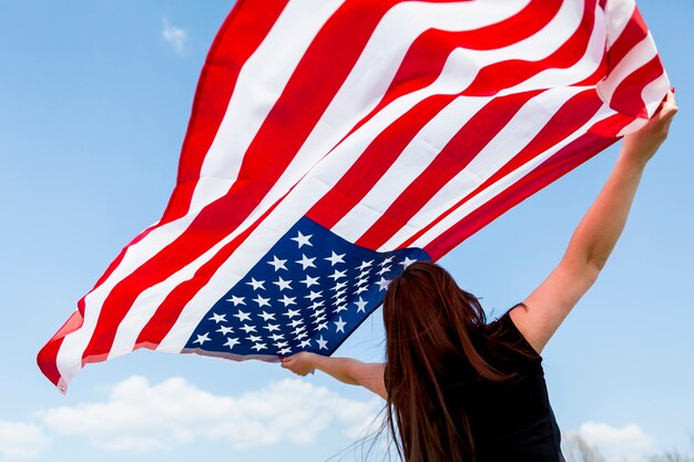 Frau, die amerikanische Flagge zum blauen Himmel anhebt