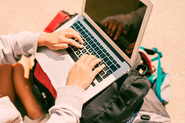 Frau, die an dem Laptop gesetzt auf Rucksäcke arbeitet