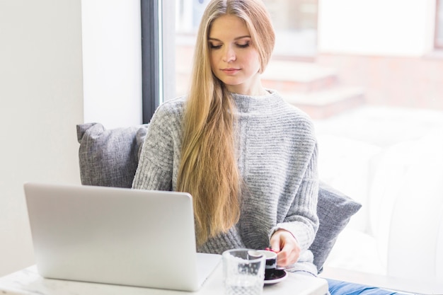 Frau, die an dem Laptop sitzt am Fenster arbeitet