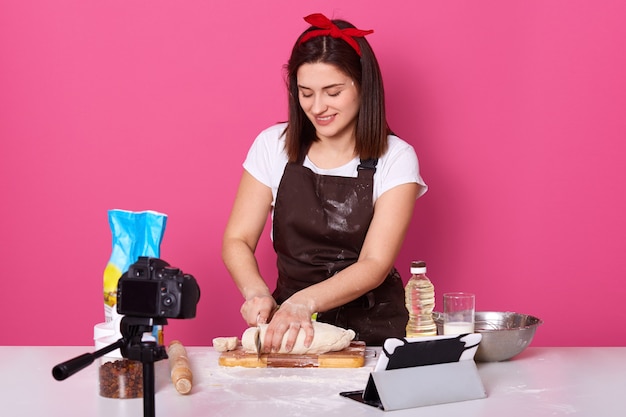 Frau, die an der Küche kocht, rohen Kuchen mit Messer schneidet, Vergnügen während des Prozesses erhält, Schüssel, Öl, Brett habend