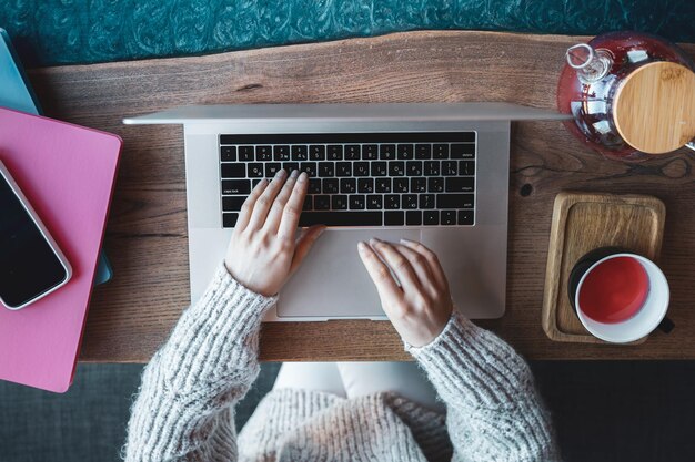 Frau, die an einem Laptop in einem Café mit Draufsicht einer Tasse Tee arbeitet