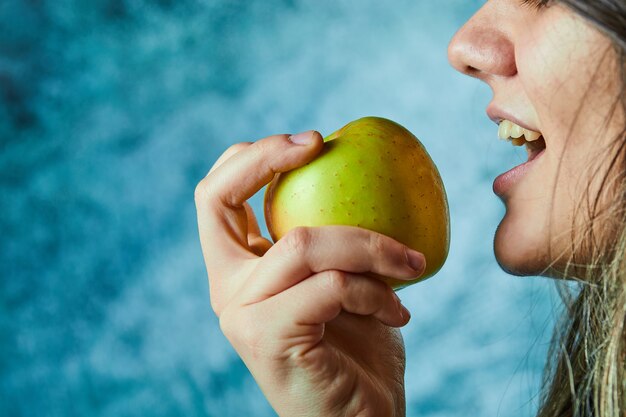 Frau, die Apfel auf blauer Wand isst.