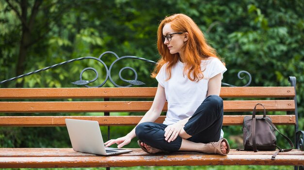 Frau, die auf Bank mit Laptop sitzt