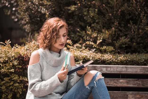 Frau, die auf Bank sitzt und Bücher hält