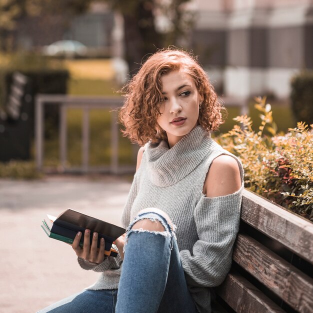 Frau, die auf Bank sitzt und geöffnetes Buch im Park hält