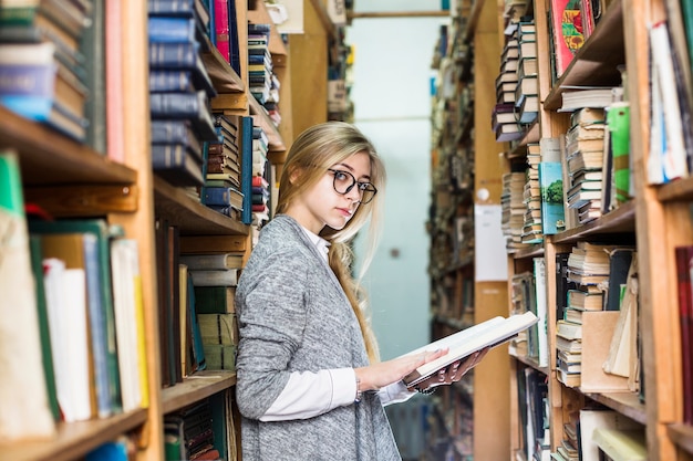 Kostenloses Foto frau, die auf bücherschrank sich lehnt und kamera betrachtet