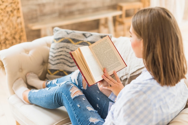 Frau, die auf Couch mit Lesebuch sitzt