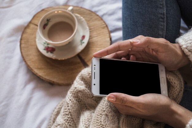 Frau, die auf Decke mit Kaffee und Smartphone sitzt