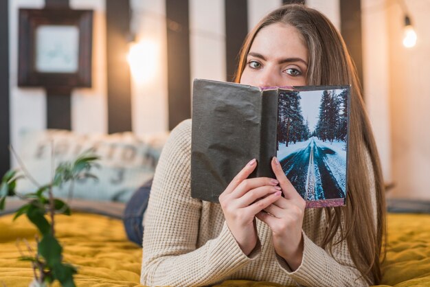 Frau, die auf dem Bett bedeckt ihren Mund mit Buch liegt