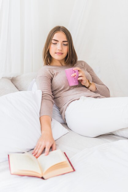 Frau, die auf dem Bett betrachtet Buch sitzt